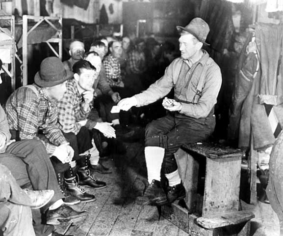 Photo of lumberjacks in a bunkhouse, one man is performing card tricks, ca. 1925.