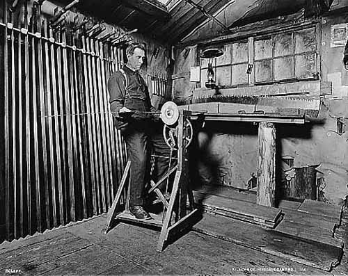 Photo taken inside the filer's quarters of the filer sharpening a long saw with a foot-powered machine, 1914.