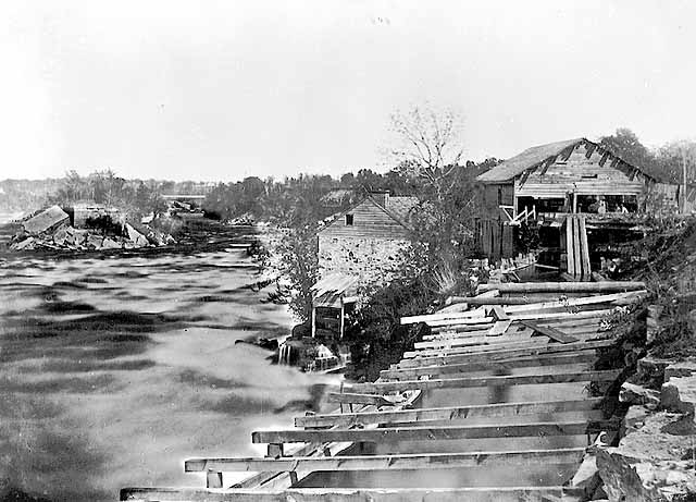 Photo of wooden mill with the Mississippi River in the foreground, 1857.