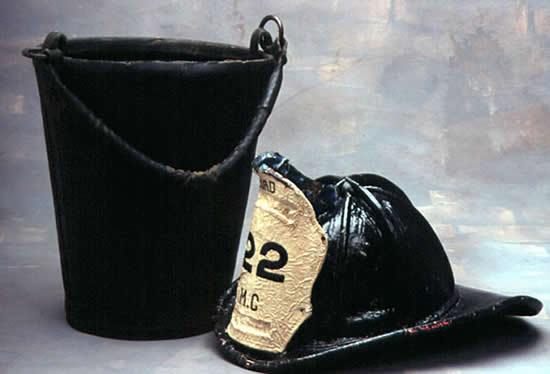 Color photo of a fireman's helmet and a leather bucket.