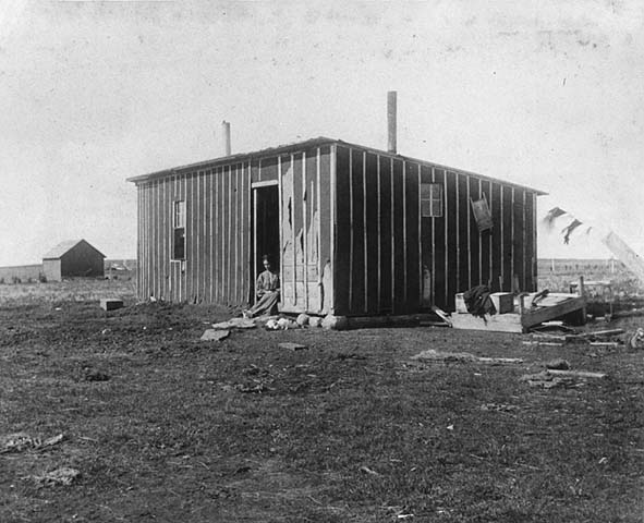Photo of a woman sitting in the doorway of a prairie shanty, ca. 1904.