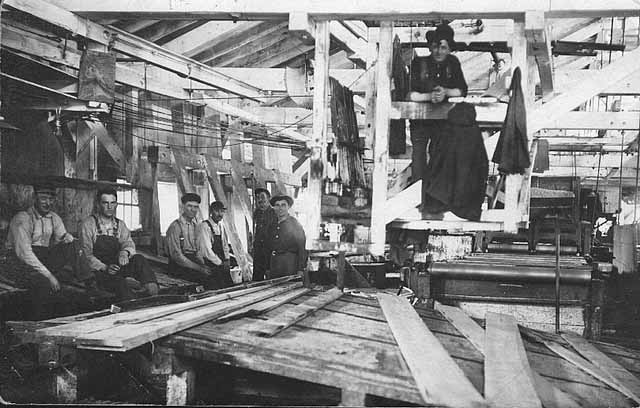 Photo of seven workers posing inside a mill, 1910.