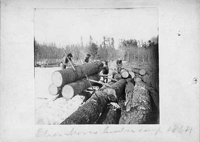 Photo of a four-person crew unloading logs from a sled onto a frozen lake, 1864.
