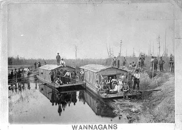 Photo of log driving crew docked with two wanigans along the banks of a river, 1885.