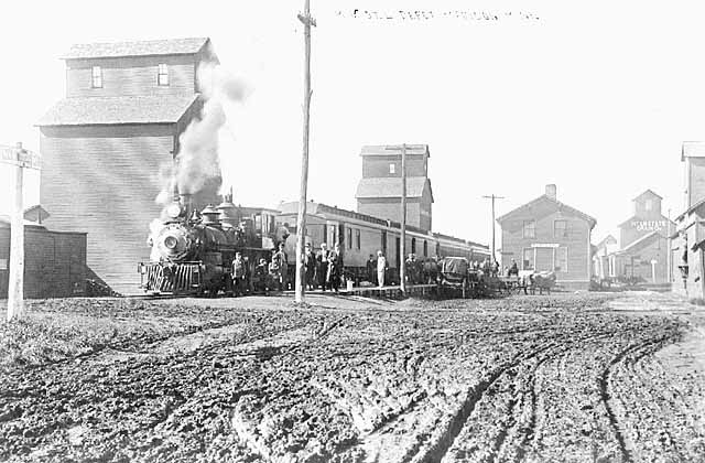 Photo of a town on Minnesota's western boarder showing dirt roads, a train, and a grain elevator, ca. 1890.