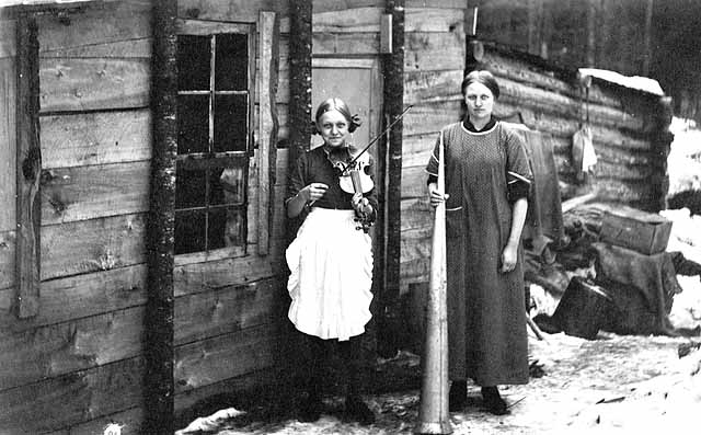 Photo of two female cooks; one holds a dinner horn and one holds a fiddle and both appear to be in their twenties, 1917.
