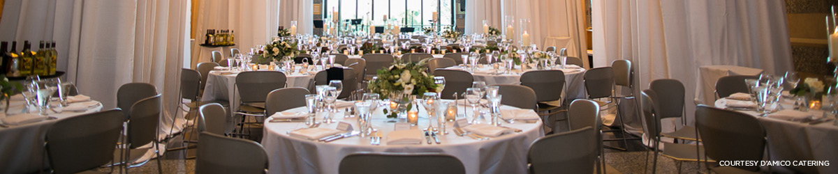 Several round tables are set with fine linens, crystal stemware, and floral centerpieces in preparation for a formal event.